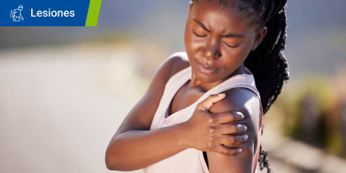 Mujer siente dolor en la zona del hombro porque tiene un desgarro muscular. Se lee el texto “Lesiones” en un recuadro. Mujer siente dolor en la zona del hombro porque tiene un desgarro muscular. Se lee el texto “Lesiones” en un recuadro.